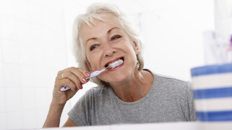 Senior Woman In Bathroom Brushing Teeth At Home